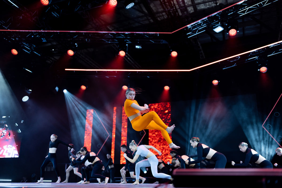 Neve Harvey mid-air during a trick on stage under red and blue lights