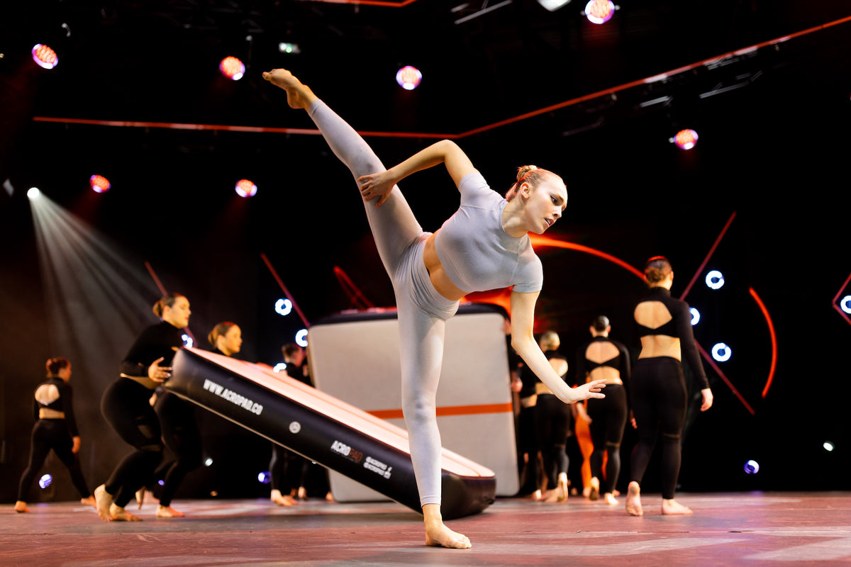 Serena McCall performing a dance extension on stage beside an AcroPAD AirTrack